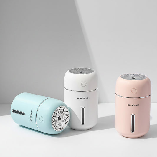 Three small humidifiers in blue, white, and pink on a light surface with a minimal background.
